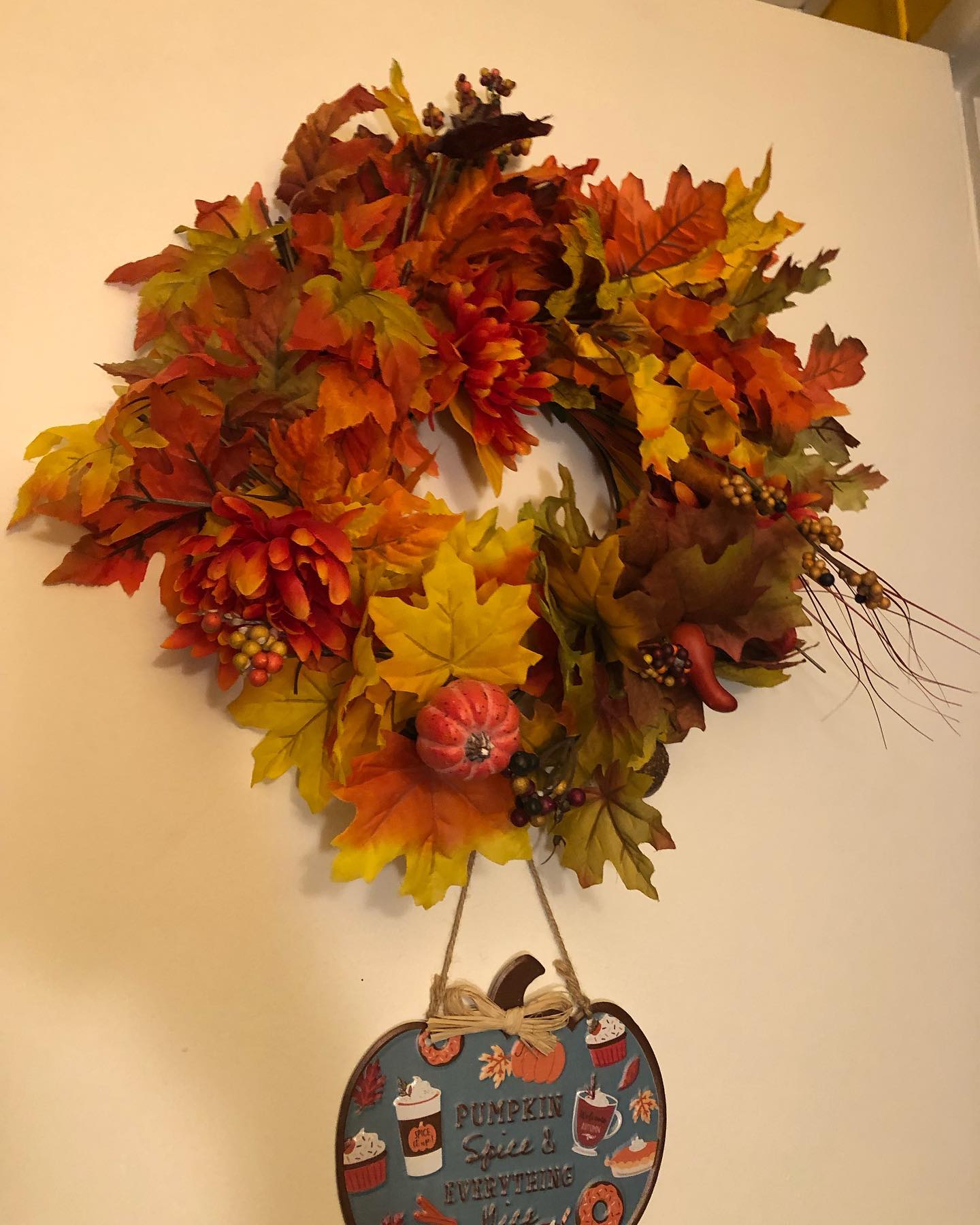 a fall wreath with artifical maple leaves, pinecones, an artificial pumpkin, and a few scattered orange flowers and seed stems.