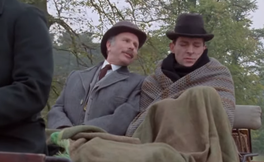 a still from the 1984 jeremy brett sherlock holmes show. holmes is wrapped in an exceptionally cozy looking beige knit blanket, while watson affectionately chides him.