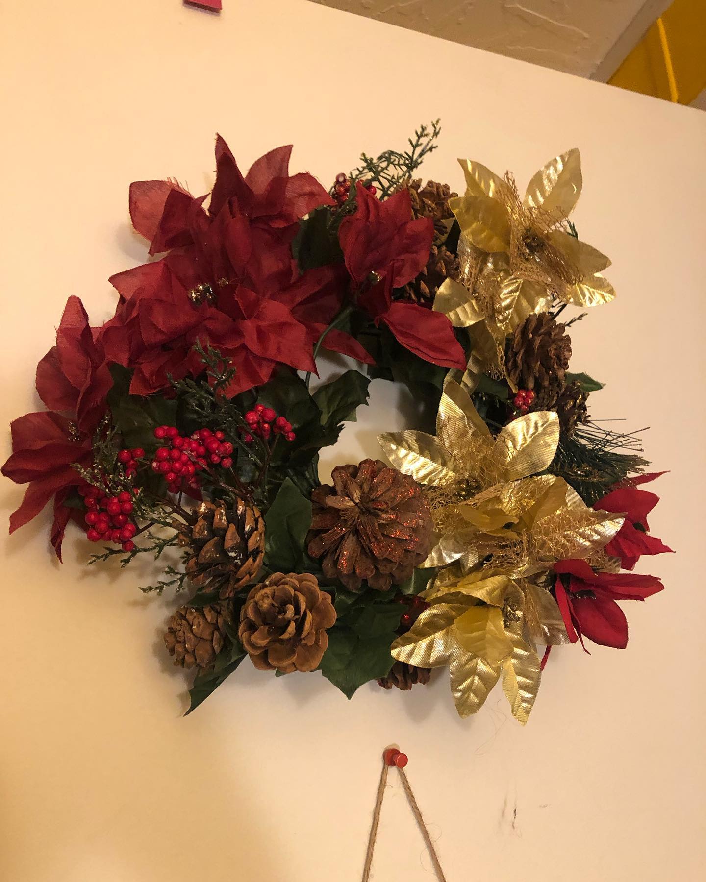 a winter wreath with artificial evergreen boughs, a few holly boughs, big pinecones, and red and gold poinsettas.